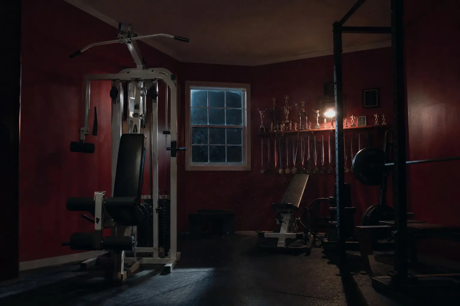Empty home gym with crimson walls, a squat rack, and a shelf of trophies