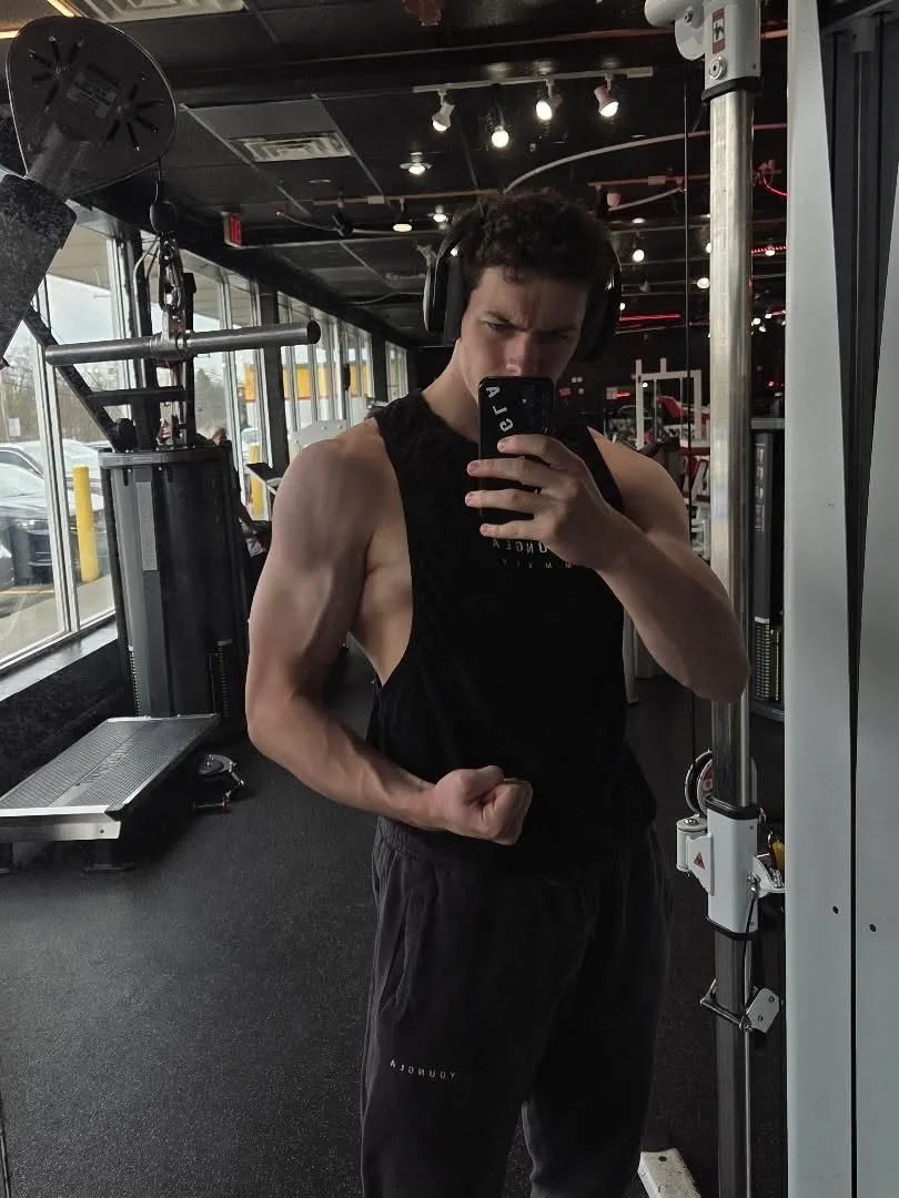 Sam in the gym, headphones on, flexing his right arm